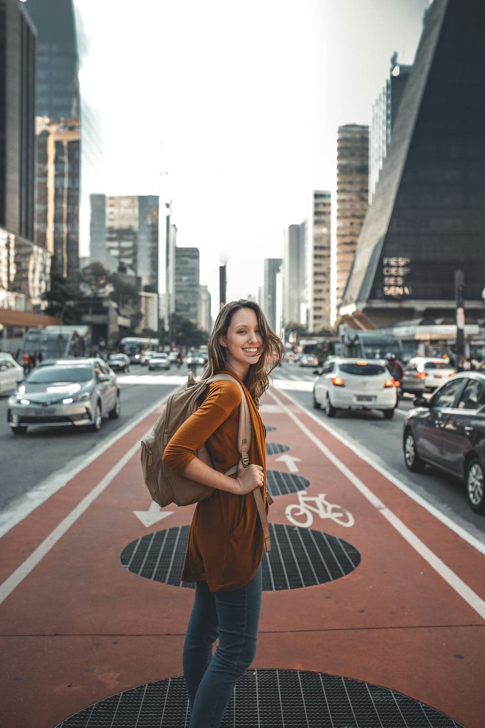 Mulher sorrindo em pé na Avenida Paulista, com trânsito ao fundo